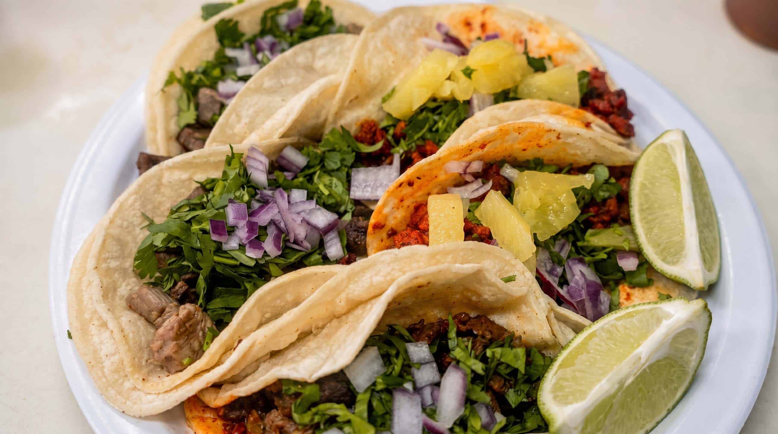 Street tacos topped with onion, cilantro, pineapple and lime